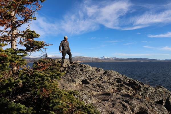 A hiker walks across a rocky outcropping above a large lake.