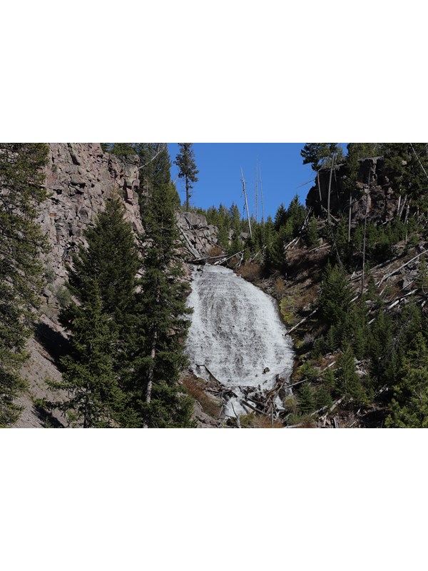 Water cascades down a slope surrounded by rocky cliffs and sparse trees.