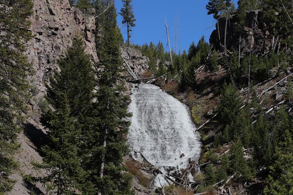 Water cascades down a slope surrounded by rocky cliffs and sparse trees.