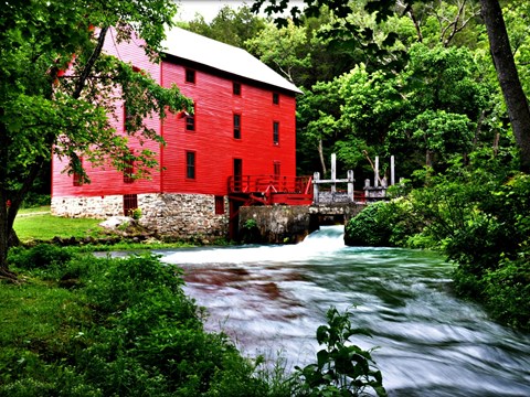 Alley Mill painted in red up close with Alley Spring flowing clear and blue from it.