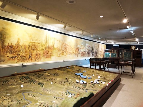A museum exhibit hall has a battlefield diorama and mural painting.
