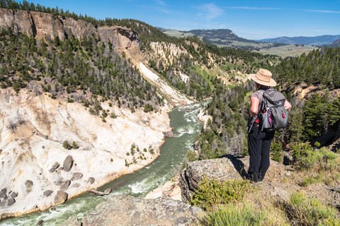 A hiker stands on the edge of a canyon and looks down at the river below.