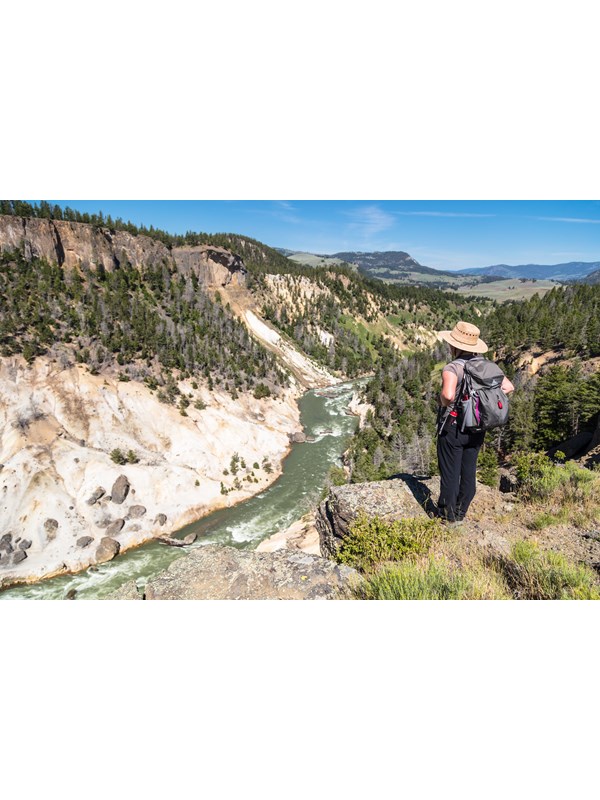 A hiker stands on the edge of a canyon and looks down at the river below.