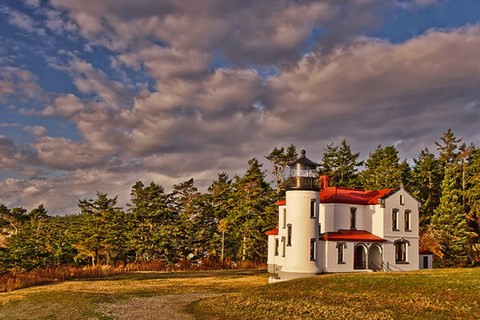 Lighthouse building on grass with forest behind.