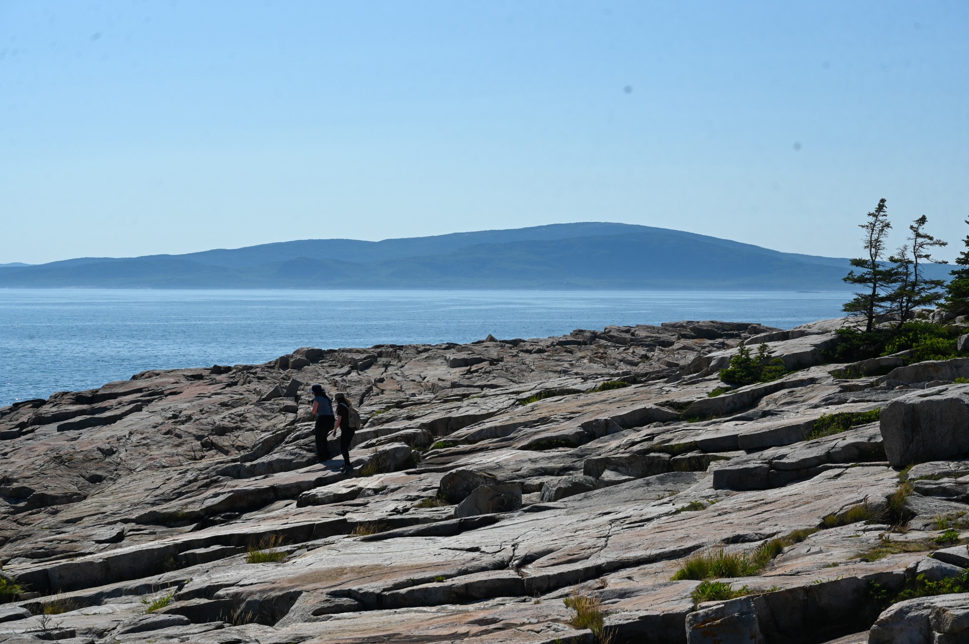Two women walking on a rocky shore with water and a mountain in the background