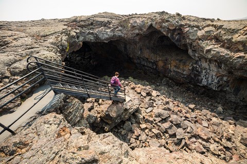 A person walks down a set out stairs into the wide open entrance of a lava tube.
