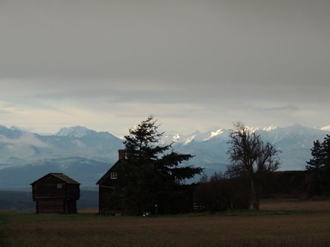 Old wood house in field with mountain range behind.