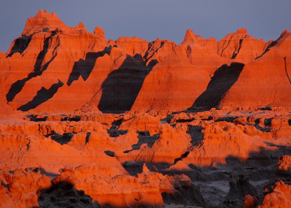 badlands buttes are illuminated by red sunlight, which creates shadows in the canyons.