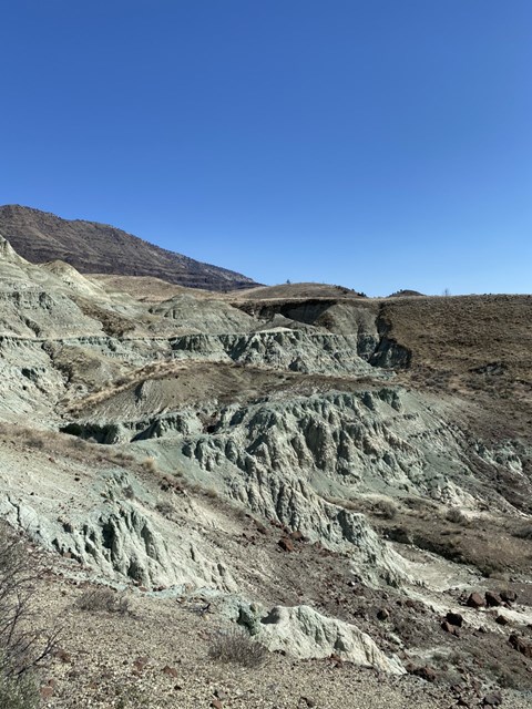 Layered blue claystone rocks in a valley with blue skies in the background