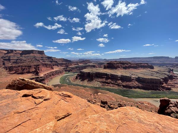 A narrow green river bends around a deep canyon on a sunny day.