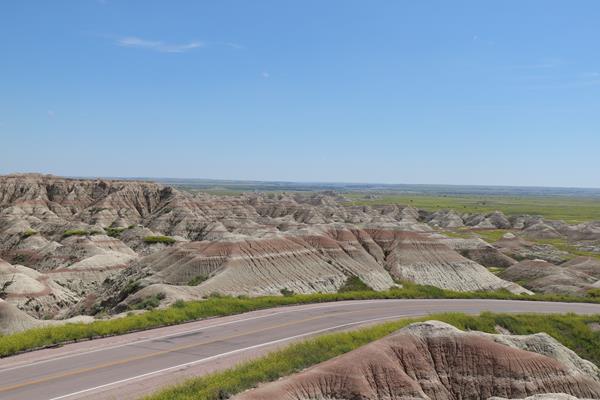 a paved road descends into a prairie landscape with buttes in the background.