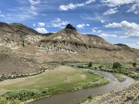 A pointed mountain with a river flowing in front through green fields