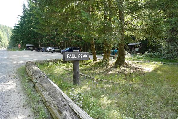A dirt road in a forest leads to a parking area on the right with a small sign reading "Paul Peak".