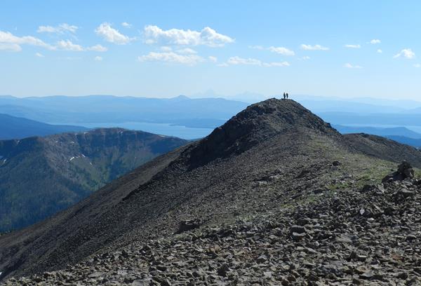 Two hikers enjoying the view of mountains in the distance from the summit of rocky mountain.