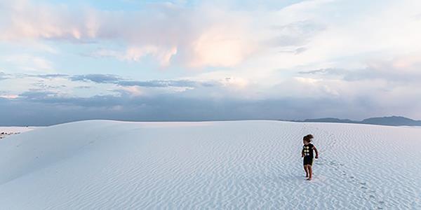 A kid leaves footprints in the sand on a partly cloudy day.