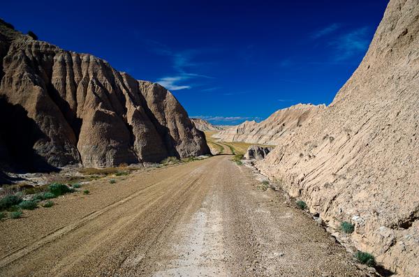 a dirt road leads between the low point of two buttes with a vibrant blue sky ahead.