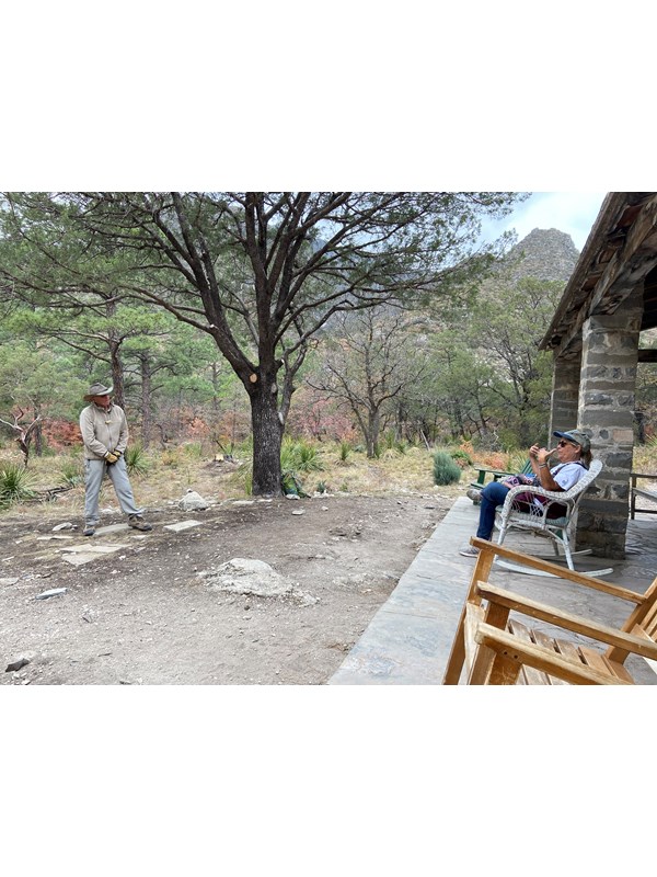 Volunteer speaks to a visitor seated on the porch of a stone cabin
