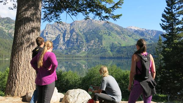 Hikers viewing a lake with mountains reflected into it.