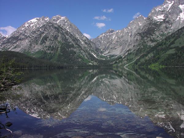 A lake mirrors the scene of mountains soaring to high elevations with a deep blue sky.