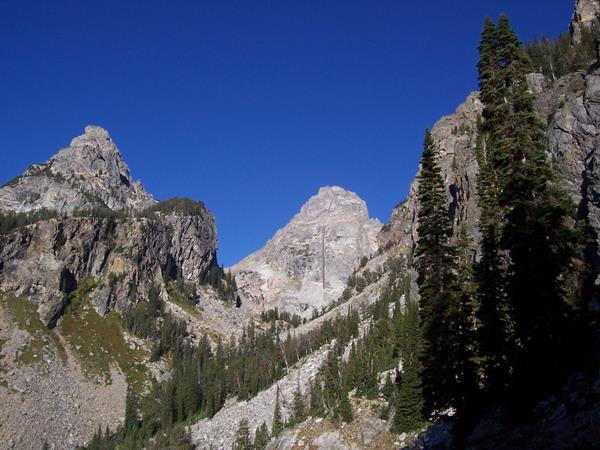 Steep mountains form a U shaped canyon. Conifers grip the mountains side at lower elevations.