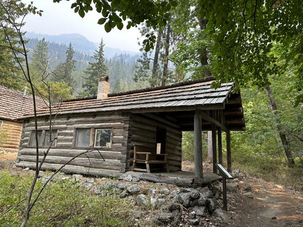 A small cabin with large covered front forch sits in a woodland