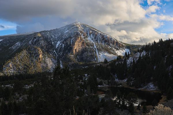 Golden hour light illuminates a small, rocky mountain with a small lake at the base of it.