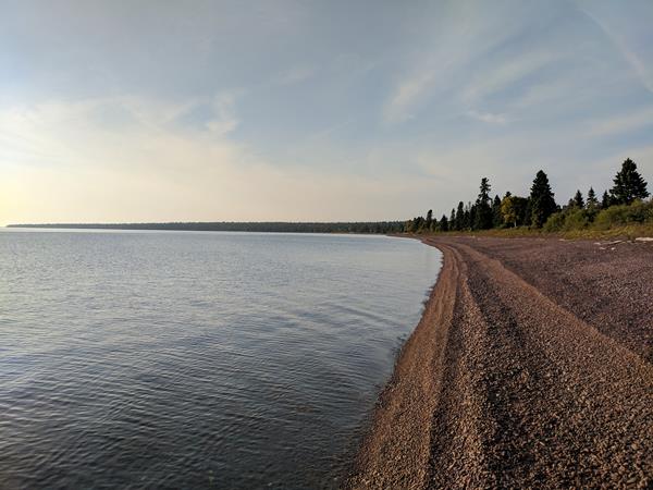 Lake Superior shoreline meets a rocky beach with trees in the distance.