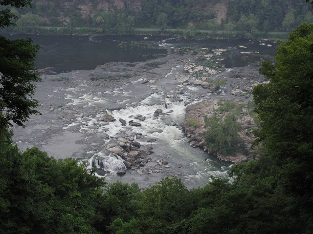Looking down onto the river and a waterfall through bright green trees.