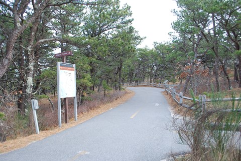 Entrance to the paved bike trail with regulation signage and trees.