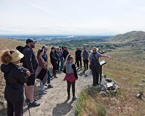 A group of people stand around a uniformed ranger pointing into the distance.