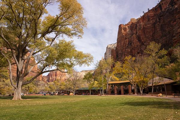 Photo of a brown building with a large grassy lawn in front of it, and mountains behind.