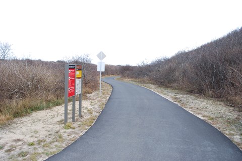 Entrance to the paved bike trail with regulation signage and bushes.