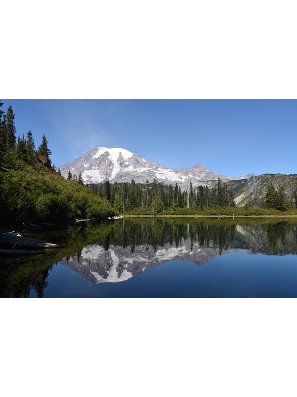 Glaciated mountain with mirrored reflection in lake with blue sky and trees