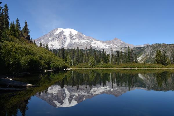 Glaciated mountain with mirrored reflection in lake with blue sky and trees