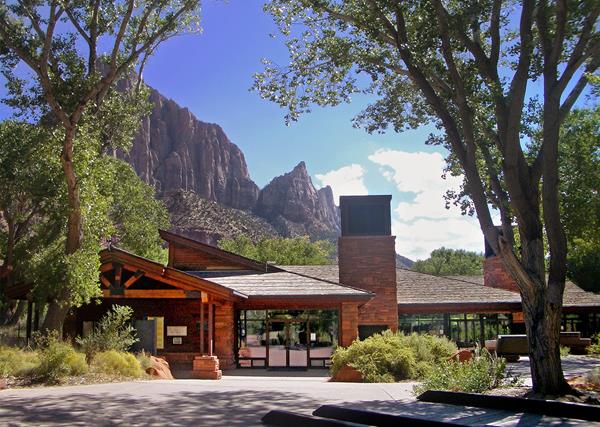 Photo of a sandstone building under a cloudy blue sky, surrounded by green trees.