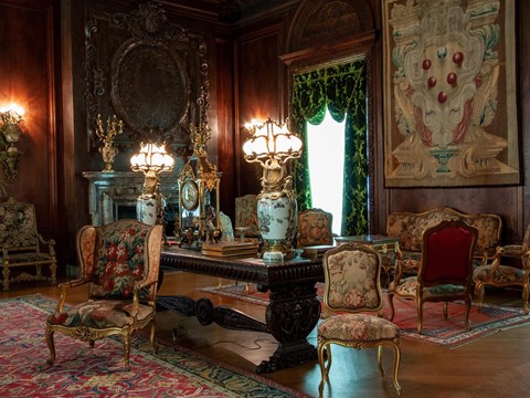 A large paneled room with a variety of furniture, carpets, and tapestries.