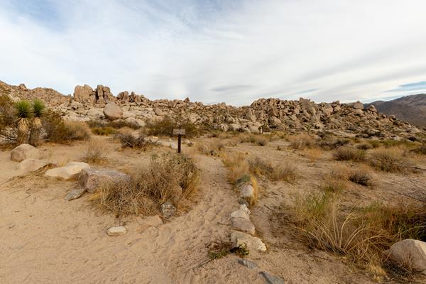 A trail sign next to a small, dirt trail, surrounded by rocks.