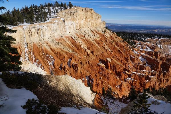 A brightly colored cliff of orange and white rock with a forested cliff above