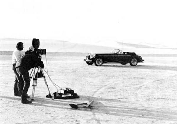 Cinematographers film a mid-1900s vehicle in the dunefield.