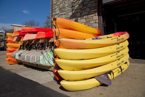 brightly colored kayaks, canoes and paddle boards are neatly stacked
