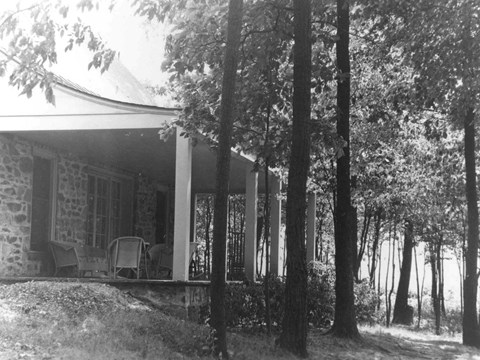 A stone house with large porch nestled among trees.