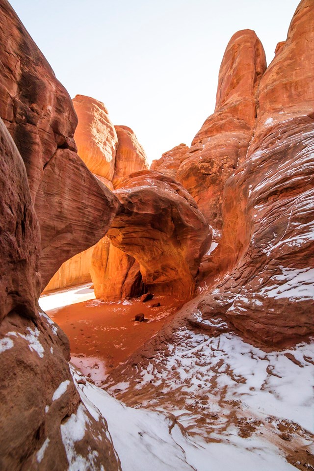 Snow on red sandstone with an arch backdropped by more sandstone walls (winter view)