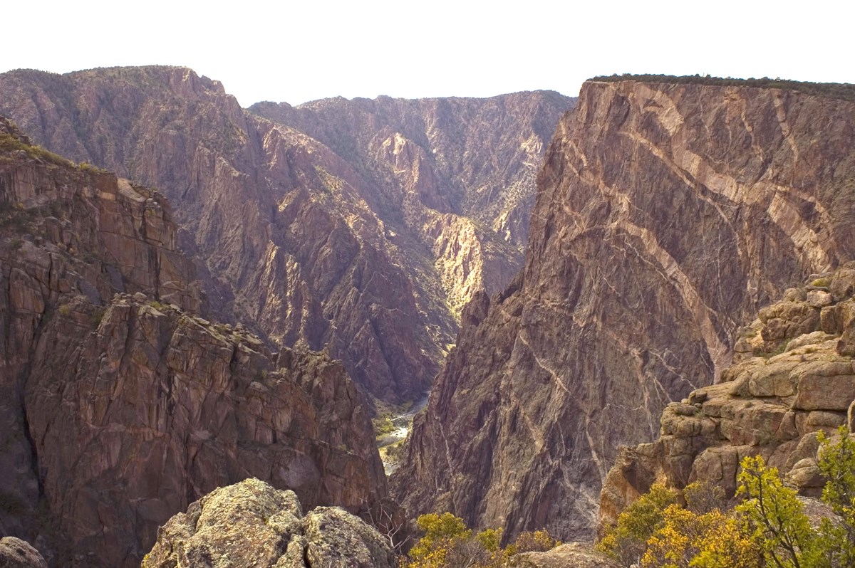 Sunlit canyon walls with pale pegmatite stripes on the Painted Wall and the Gunnison River far below