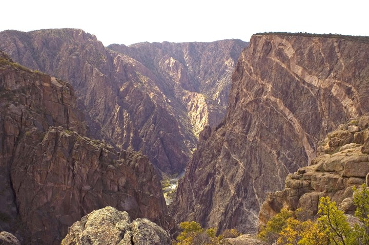Sunlit canyon walls with pale pegmatite stripes on the Painted Wall and the Gunnison River far below