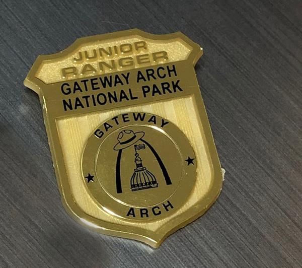 a shiny golden badge that says Gateway Arch National Park Junior Ranger