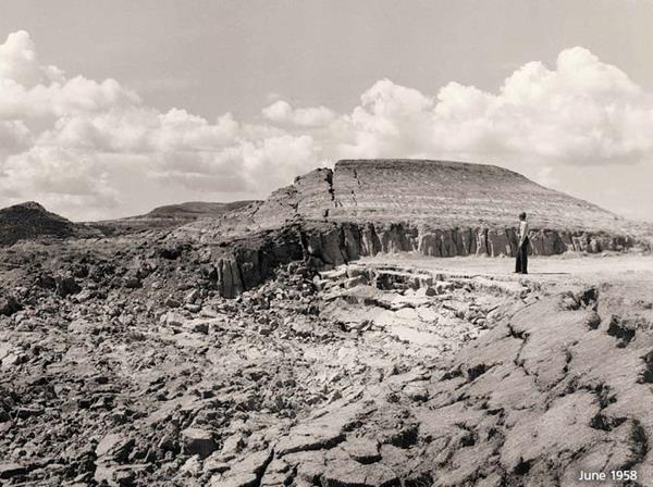 A black and white photo of a person standing at the edge of a collapse caused by a burning coal seam