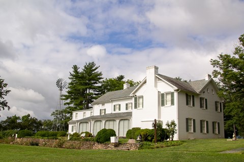 A white brick home sits underneath a blue sky with green grass and plants in the foreground
