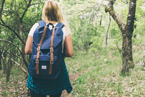 a woman with blonde hair and blue backpack walking away on a trail in the woods