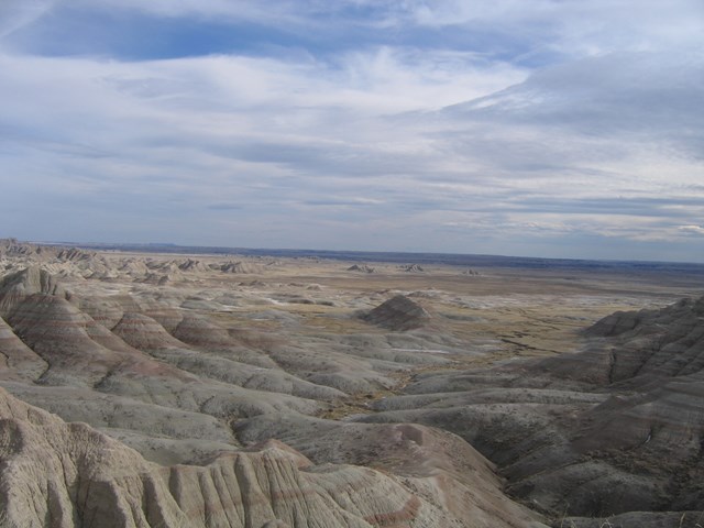 Rolling badlands buttes extending to the horizon under a hazy blue sky
