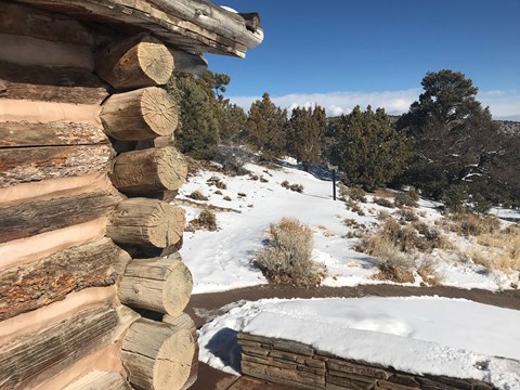 The edge of a log cabin with large beams sits to one side, with a trail stretching forward in snow